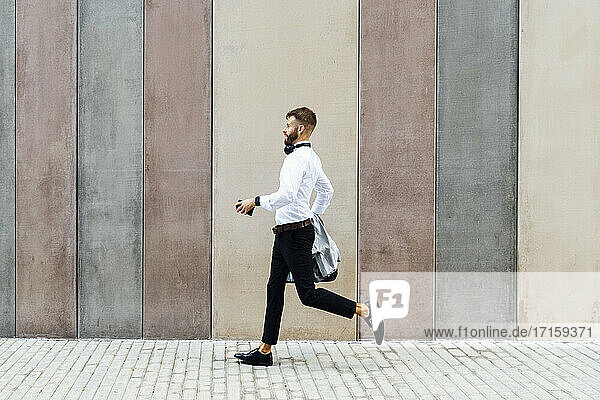 Businessman holding briefcase and jacket while running against wall