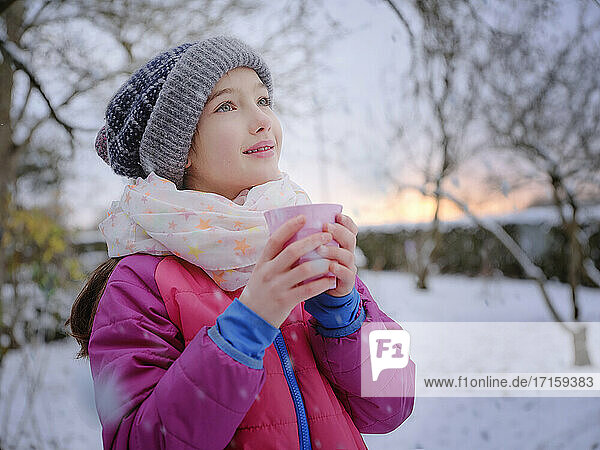 Thoughtful girl holding tea cup wearing warm clothing during sunset in winter