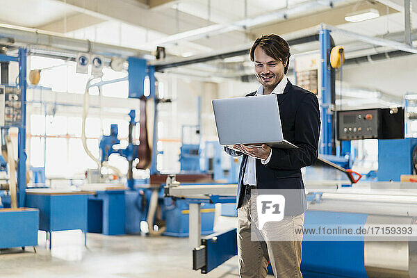 Young entrepreneur using laptop while standing at industry