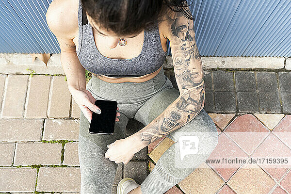 Mittlere erwachsene Frau  die ein Mobiltelefon benutzt  während sie auf dem Gehweg sitzt