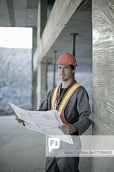Mature male construction worker with map standing at construction site