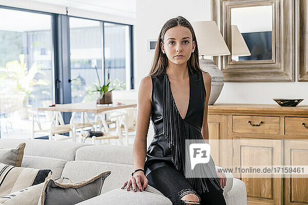 Stylish confident teenage girl wearing black top sitting on sofa in living room