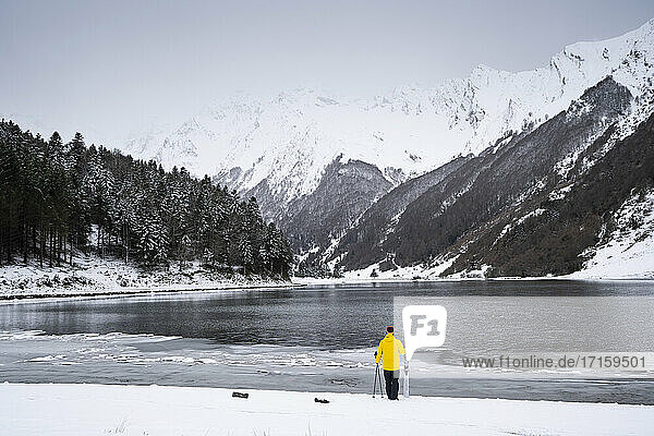 Man with ski at snow covered lakeshore in front of mountains