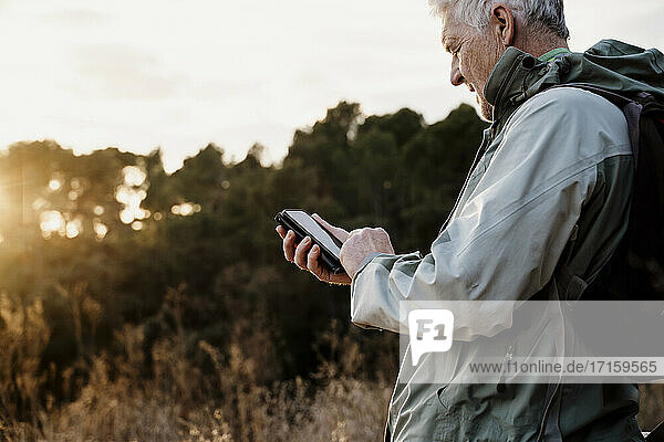 Älterer Mann benutzt sein Smartphone bei Sonnenuntergang