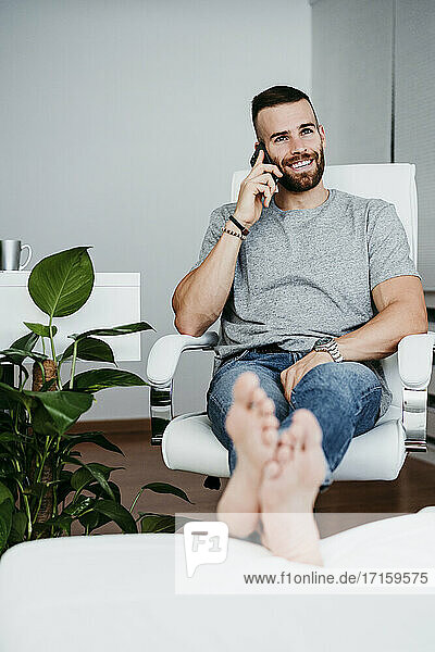 Smiling young man talking on mobile phone while working at home