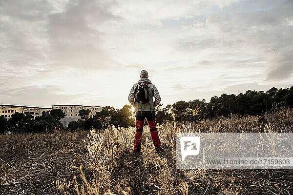 Senior male hiker standing on agricultural field at countryside during sunset