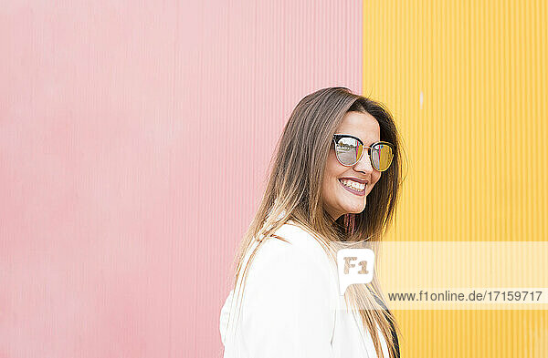 Beautiful woman in sunglasses against pink and yellow wall