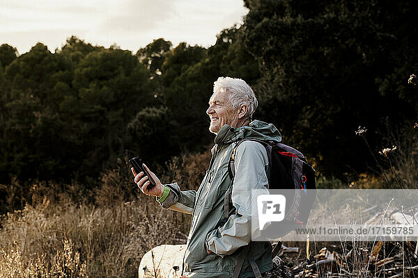 Smiling senior man with mobile phone looking away while standing in filed during weekend