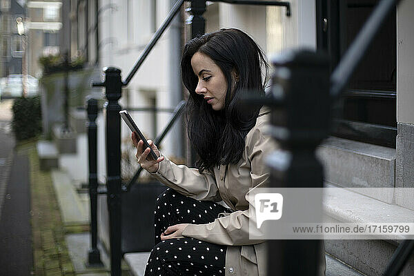Woman using smart phone while sitting on steps of house