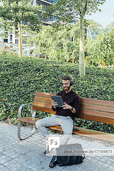 Businessman wearing headphones using digital tablet while sitting on bench