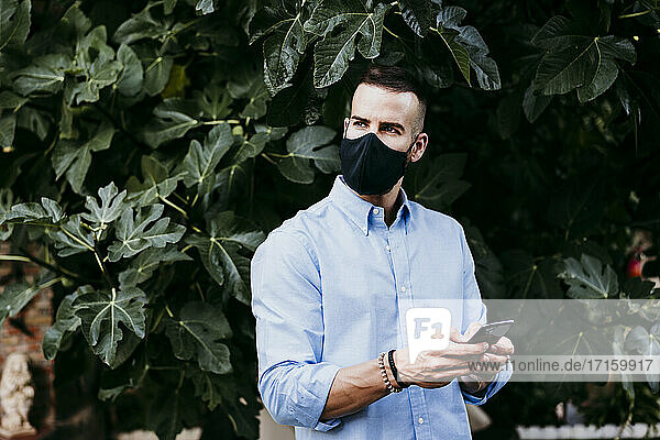 Junger Mann trägt eine Schutzmaske und benutzt ein Mobiltelefon
