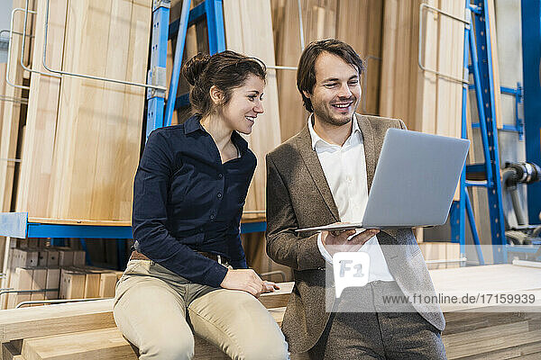 Smiling businessman using laptop while standing by colleague at industry