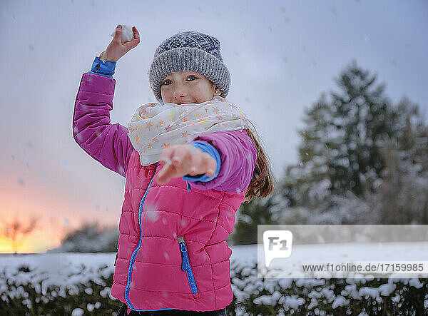 Playful girl throwing snowball in snow during winter