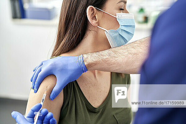 Mature female patient taking vaccination on arm while wearing protective face mask at clinic