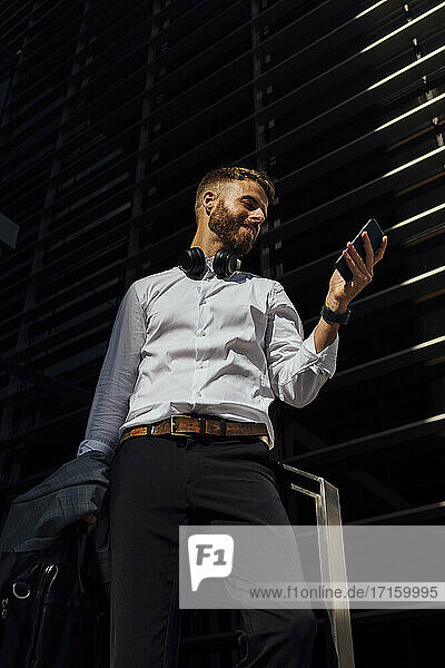 Businessman using mobile phone while standing against building