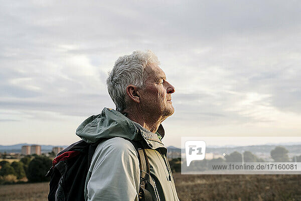 Senior male hiker with eyes closed at countryside during sunset