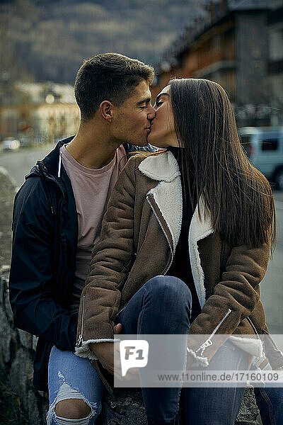 Junges Paar  das sich mit geschlossenen Augen küsst  während es in der Stadt sitzt