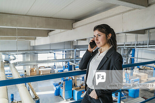 Young entrepreneur talking on mobile phone while standing at industry
