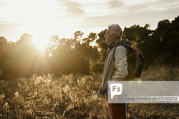 Älterer männlicher Wanderer mit Händen in den Taschen auf einem landwirtschaftlichen Feld bei Sonnenuntergang