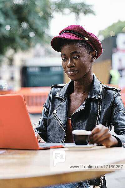 Fashionable woman drinking coffee while using laptop sitting at sidewalk cafe