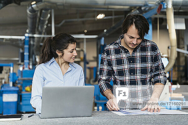 Businesswoman with laptop discussing over document while standing by colleague at industry