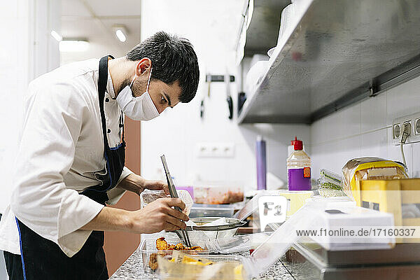 Männlicher Koch bei der Zubereitung von Speisen in Plastikbehältern in der Küche eines Restaurants während COVID-19