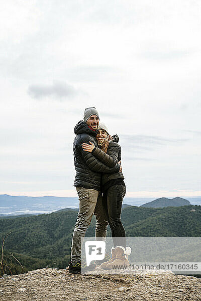 Glückliches Paar umarmt einander am Aussichtspunkt gegen den Himmel