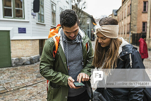 Heterosexuelles Paar navigiert durch Karte auf Smartphone in der Stadt