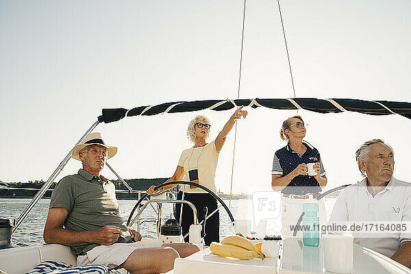 Ältere Frau zeigt  während Freunde in Segelboot gegen klaren Himmel wegschauen
