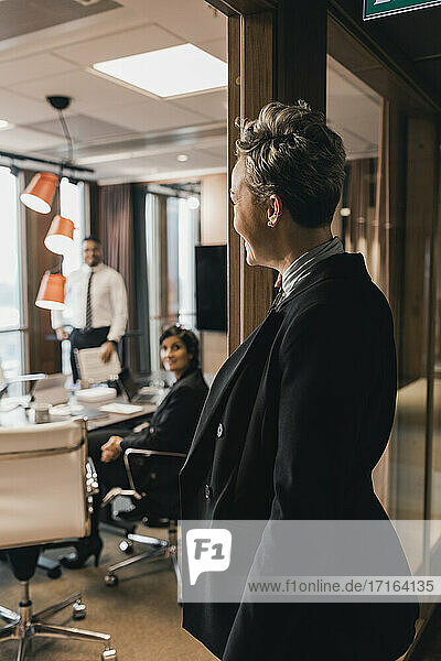 Side view of mature businesswoman looking at colleagues in board room through glass wall