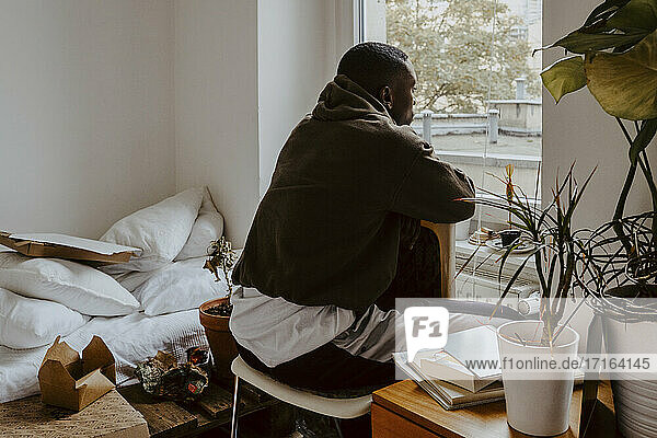 Rückansicht Mann schaut durch das Fenster  während er im Schlafzimmer sitzt