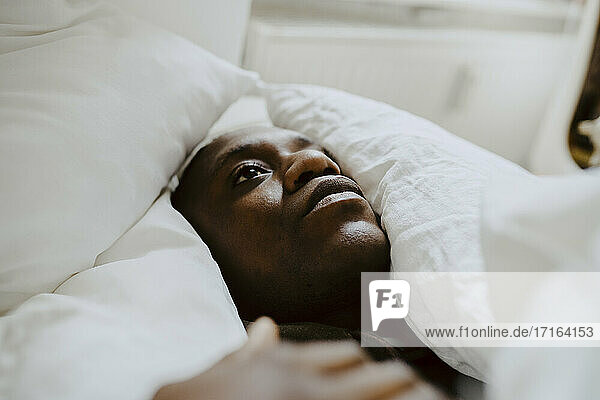 Depressed man lying amidst pillow in bedroom
