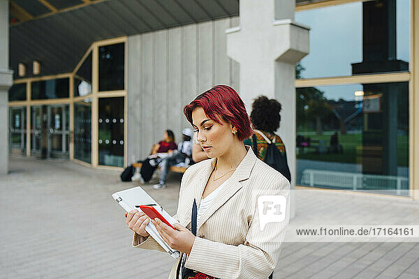 Rothaarige Studentin mit Smartphone auf dem Universitätscampus