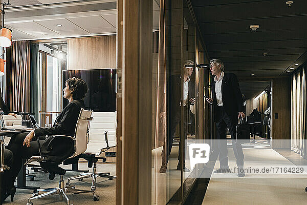 Neugieriger Geschäftsmann  der während einer Besprechung durch die Glaswand auf Kollegen im Vorstandszimmer schaut