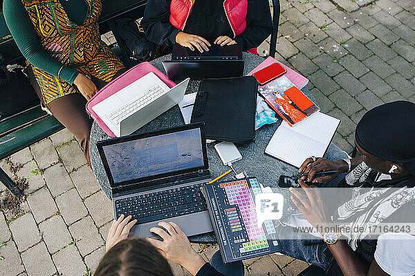 High angle view of male and female students e-learning on laptop at table in university