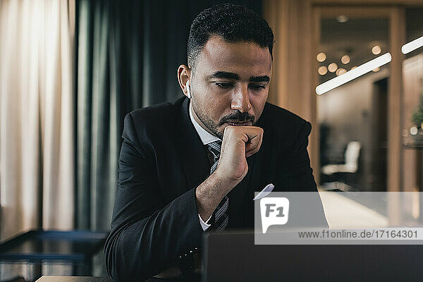 Tensed businessman looking at laptop while sitting in board room