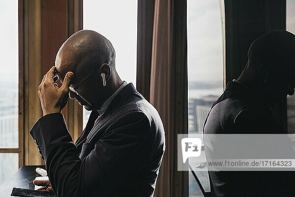 Worried male entrepreneur wearing in-ear headphones looking at smart phone in board room