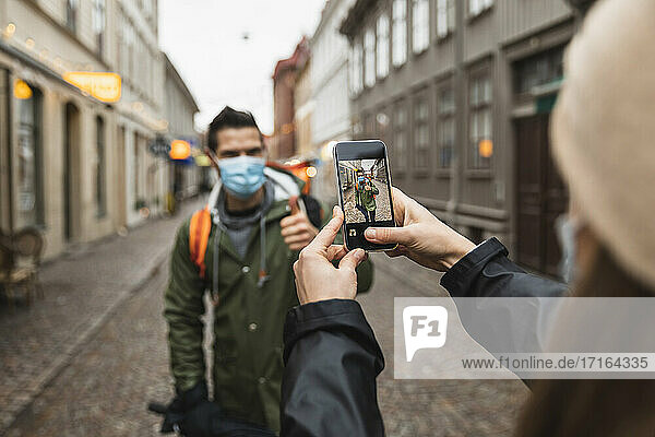 Ausgeschnittenes Bild einer Frau  die einen Mann während der Pandemie mit dem Smartphone fotografiert