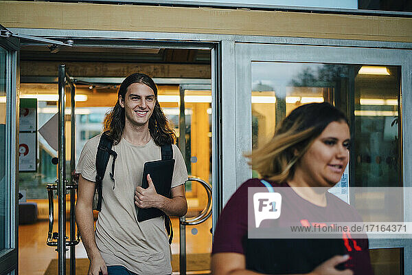 Lächelnder männlicher Student mit digitalem Tablet auf dem Universitätscampus