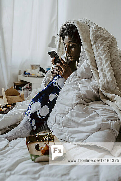 Junge Frau Text-Messaging über Smartphone beim Sitzen auf dem Bett zu Hause