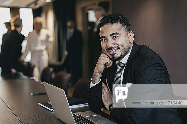 Portrait of smiling male professional sitting with laptop in board room