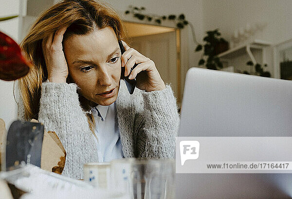 Reife Geschäftsfrau mit Hand im Haar im Gespräch auf Smartphone zu Hause