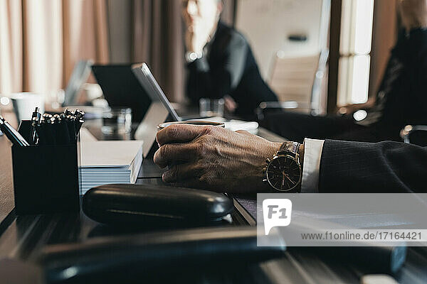 Hand eines älteren Geschäftsmannes hält Kaffeetasse am Konferenztisch im Sitzungssaal während der Sitzung