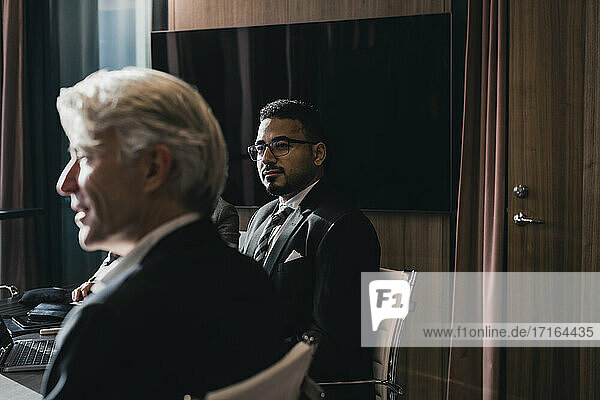 Selbstbewusste Geschäftsmann sitzt mit älteren männlichen Kollegen im Sitzungssaal während der Sitzung