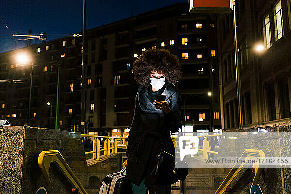 Frau mit Gesichtsmaske  die auf ihr Telefon schaut  auf Reisen in der Nacht