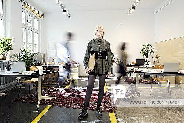 Young woman standing in busy creative co-working space