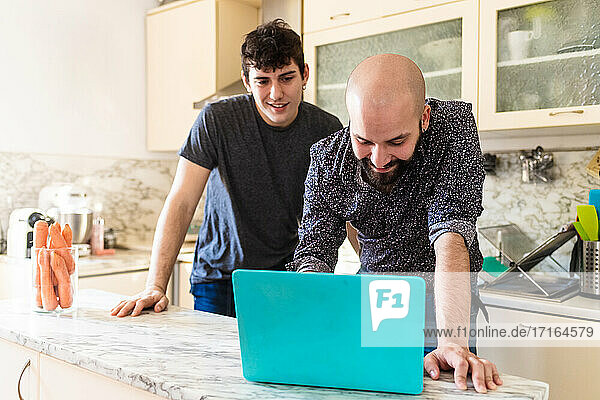 Young men looking at laptop on kitchen