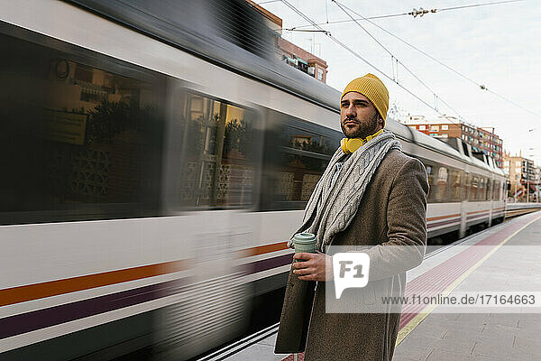 Mann mit Kaffeetasse  der wegschaut  während er auf dem Bahnhof steht