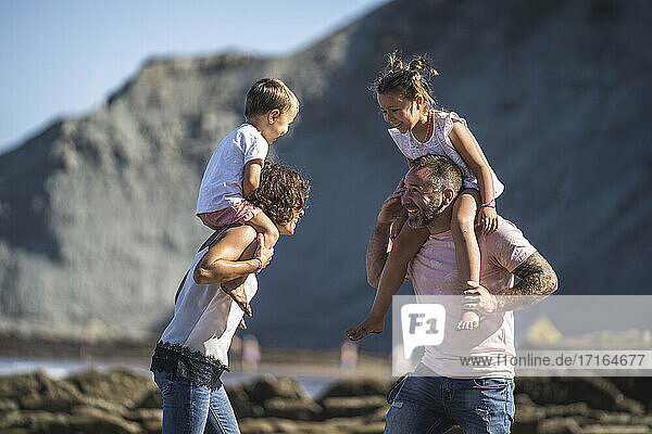 Cheerful parents carrying children on shoulder at beach
