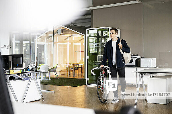 Lächelnder Geschäftsmann mit Fahrrad in einem Großraumbüro